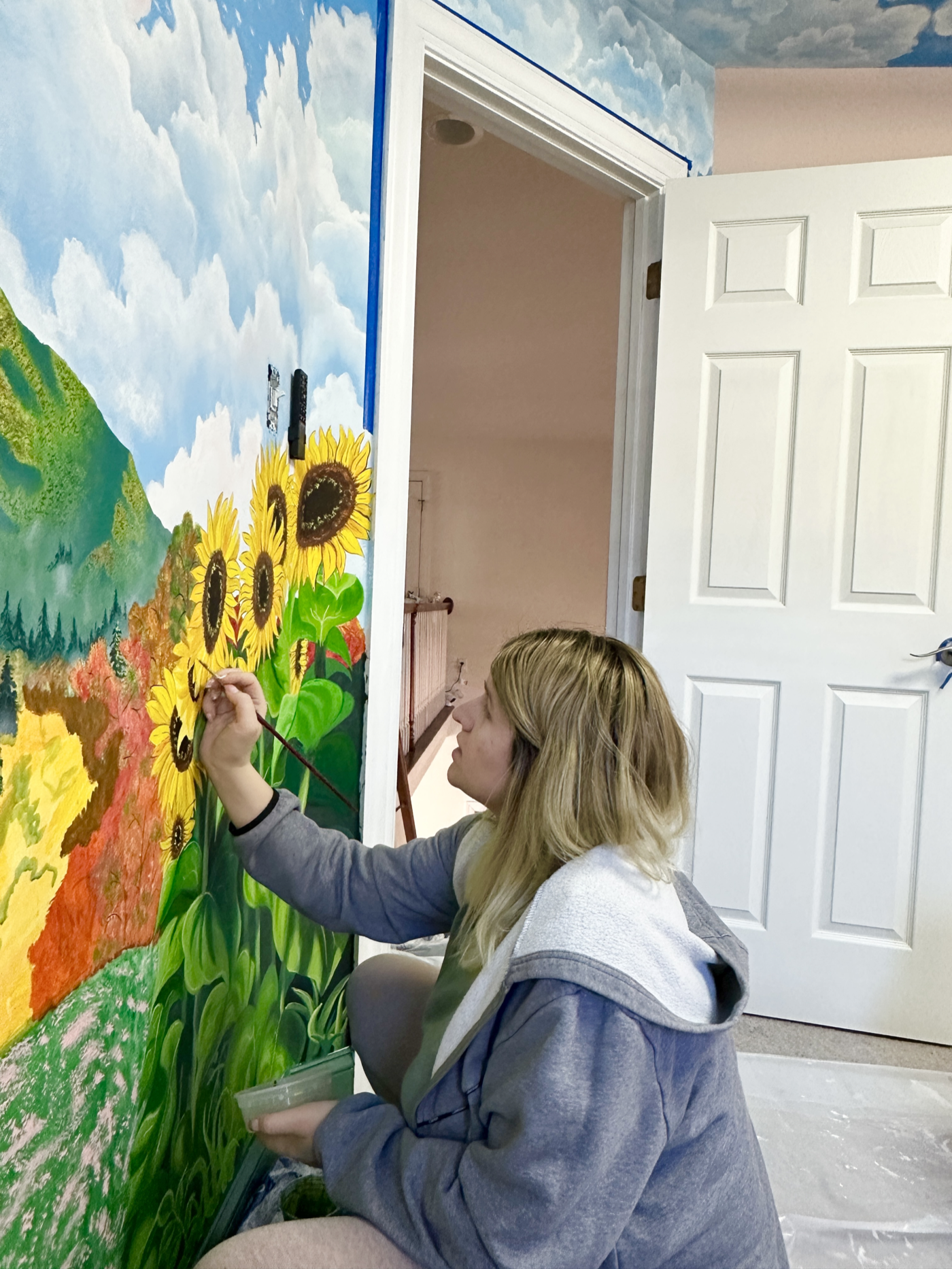 Artist painting sunflower details on a mural wall